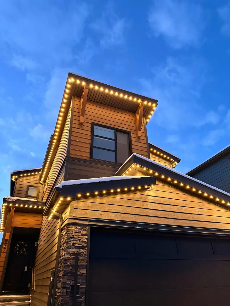 Timber home at blue hour with warm white accent lighting under snow-dusted gables