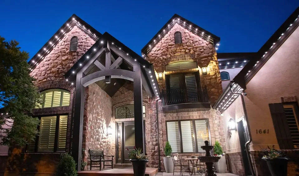 Stone craftsman home at blue hour with warm white permanent lighting along every gable
