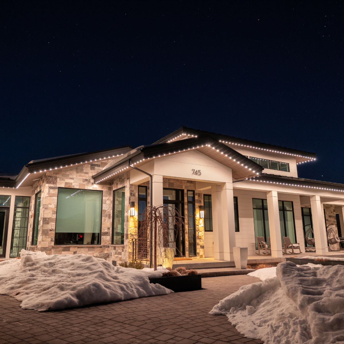 Soft white permanent LED roofline lighting on Calgary home with stone facade