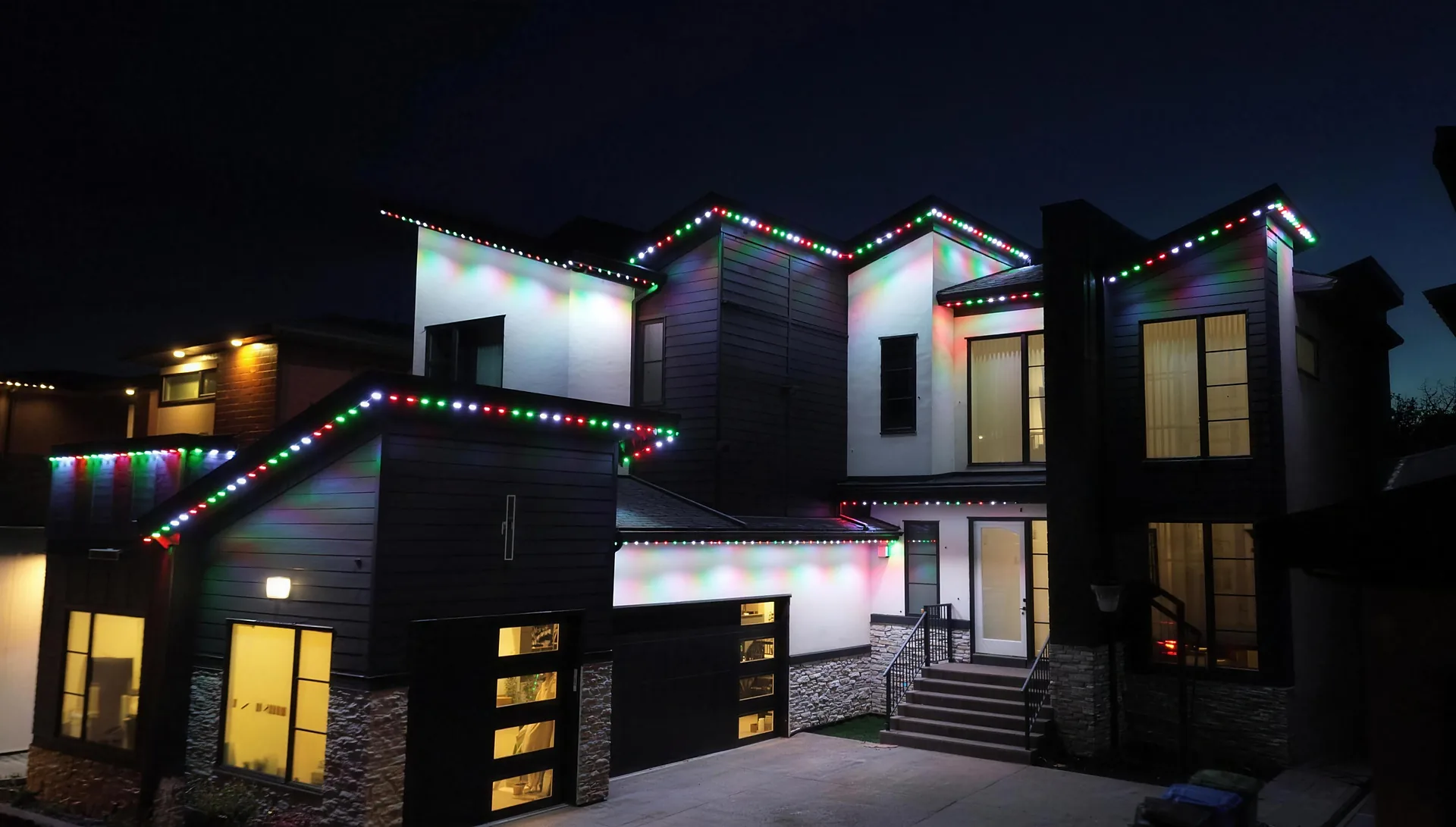 Permanent Christmas lights installed on a modern Calgary home: red, green and white LEDs along every roofline by Starise Lighting