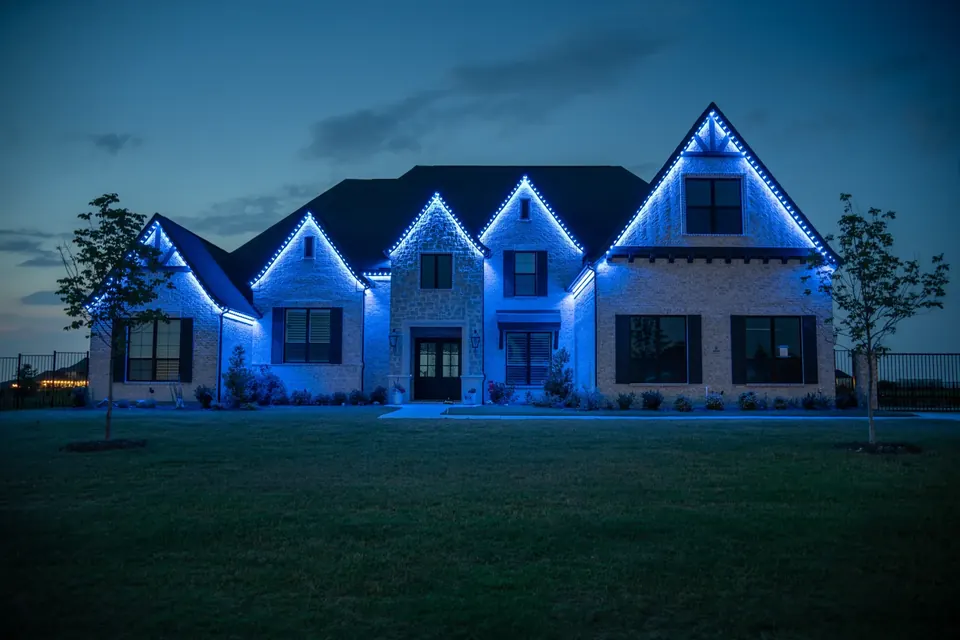 Large two-storey home at dusk with permanent lighting set to blue along its peaked rooflines