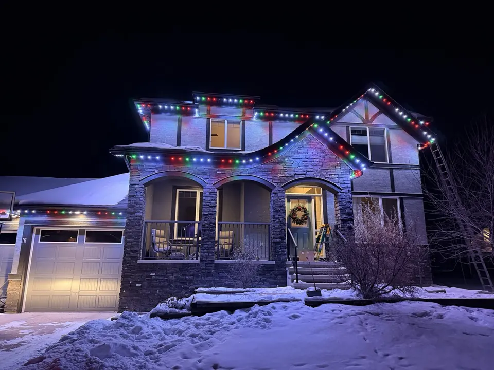 Stone Calgary home in winter with multi-colour permanent Christmas lighting on every roofline