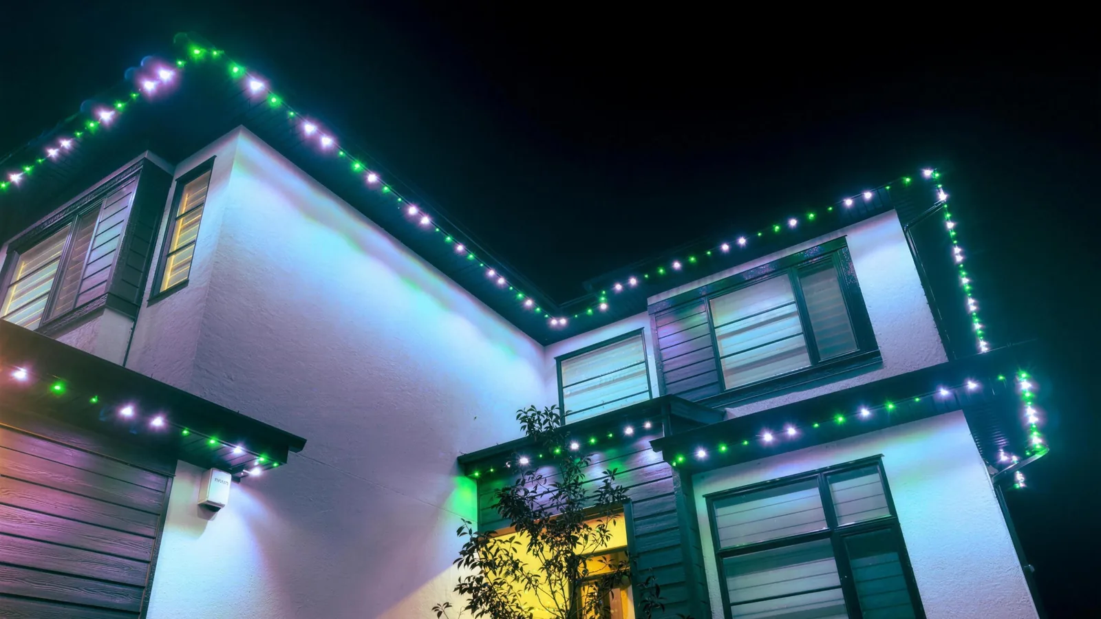 Modern two-storey home at night with green and white permanent lighting along every roofline