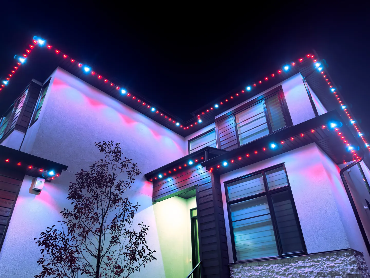 Modern two-storey home at night lit red and white along every roofline for Canada Day