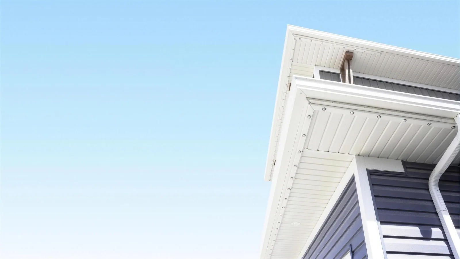 Permanent lighting installed along a white soffit and fascia, seen from below against a clear blue sky